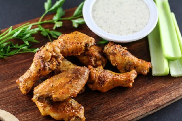 buffalo ranch chicken wings sitting on a wooden cutting board. There is parsley garnishment behind the wings and a bowl of dairy-free ranch dressing sitting nearby.