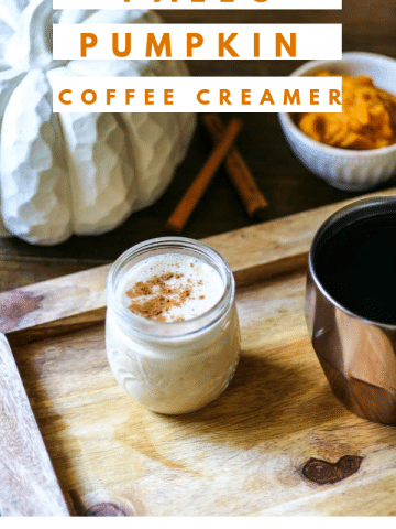 a small jar of paleo pumpkin coffee creamer sitting on a wooden cutting board. There is a cup of coffee next to it.