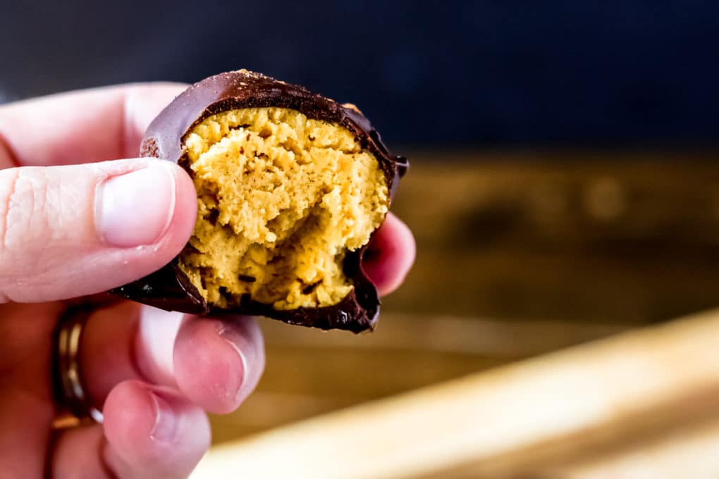 a woman holding a chocolate pumpkin truffle with a bite taken out of it