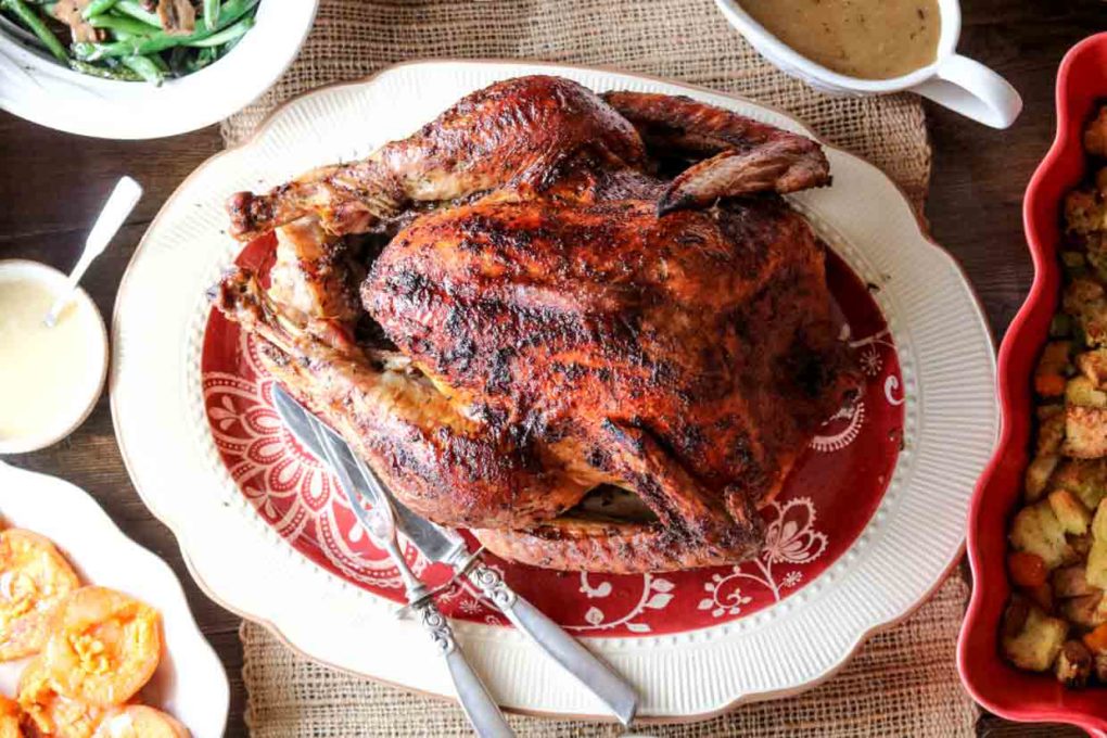 a Thanksgiving maple herb turkey on a platter setting on the table with side dishes