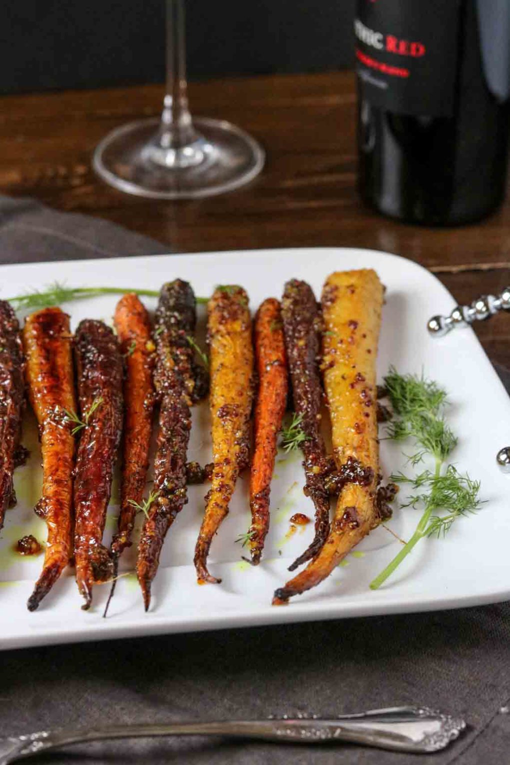 a platter of maple mustard roasted carrots with a glass of wine in the background