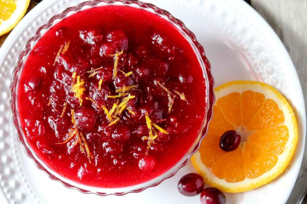 a bowl of orange cranberry sauce garnished with fresh cranberries and orange slices