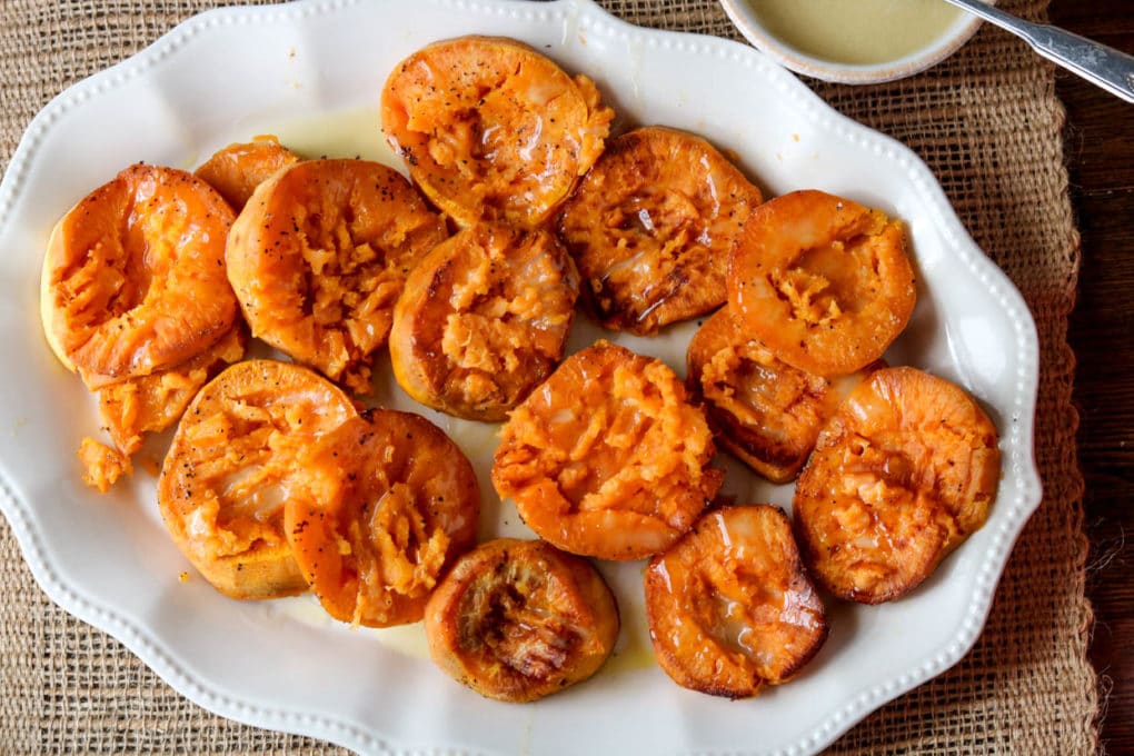 a white platter of smashed sweet potatoes with a bowl of maple aioli 