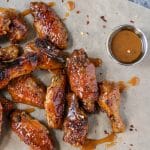 Hot Honey Mustard Wings laying on brown parchment paper with a small cup of hot honey mustard sauce sitting nearby