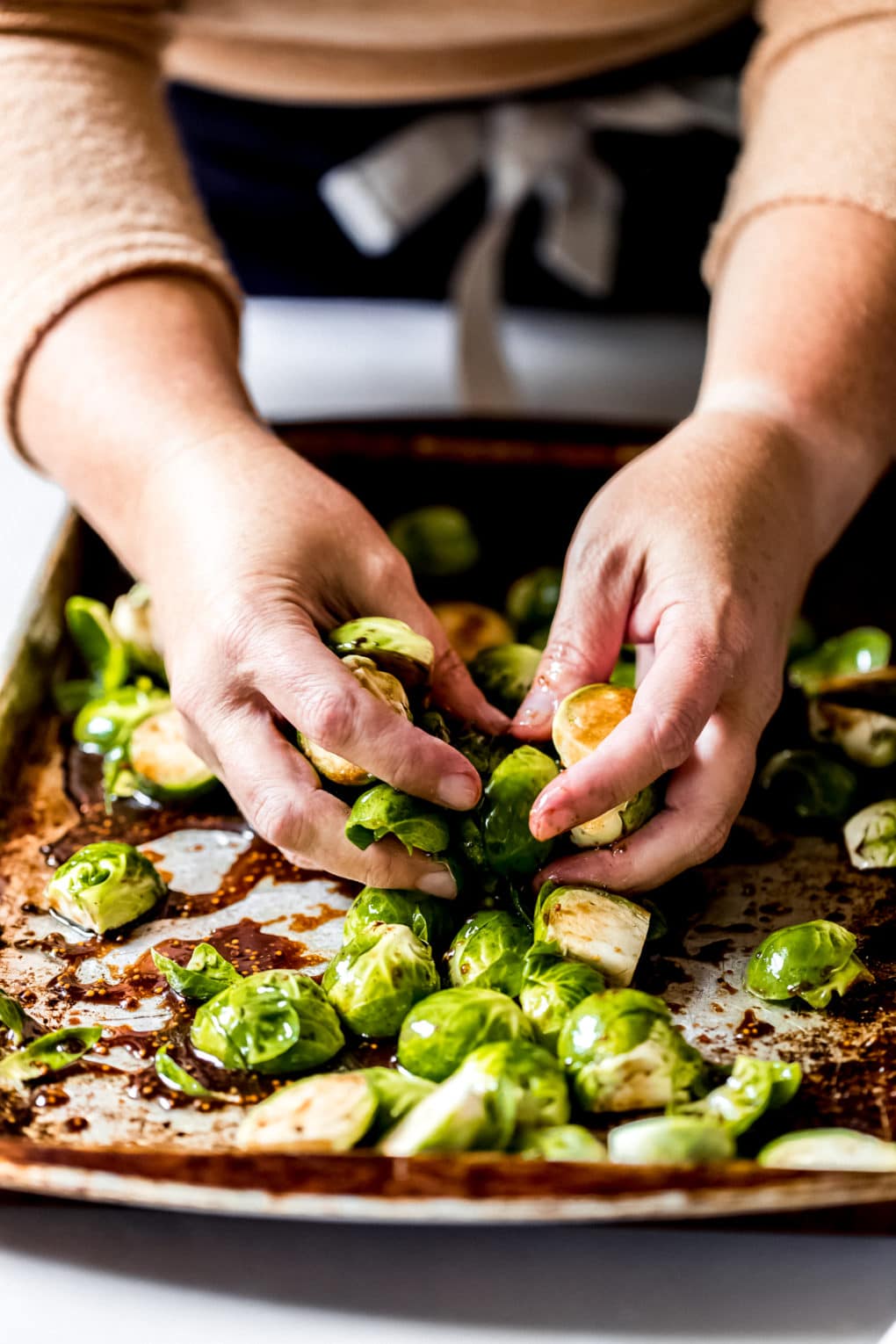 a woman hand-mixing the raw brussel sprouts with the glaze for caramelized brussel sprouts