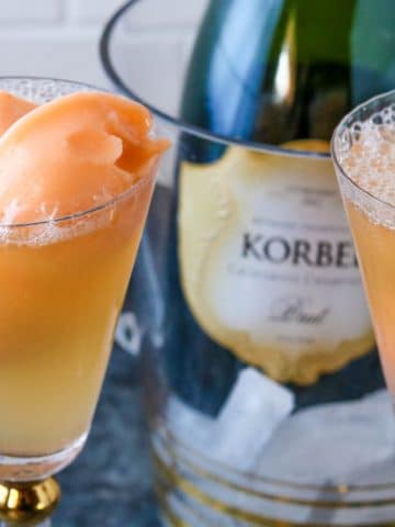 two glasses of orange sherbet champagne floats with a bottle of champagne in the background