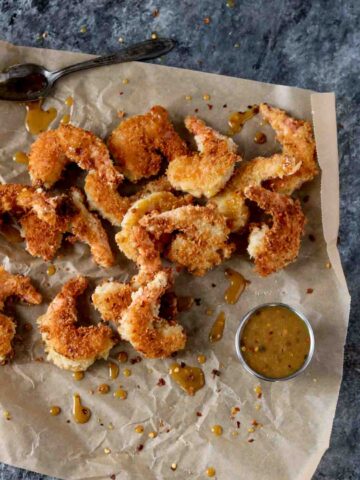 Coconut Shrimp with Spicy Honey Mustard Sauce laying on brown parchment paper with a cup of spicy honey mustard sauce sitting nearby