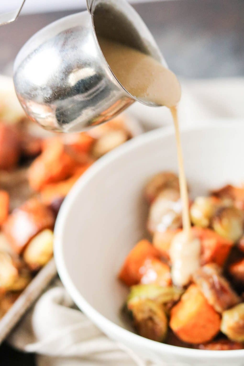 someone pouring maple tahini over a bowl of pan-roasted vegetables and sausage