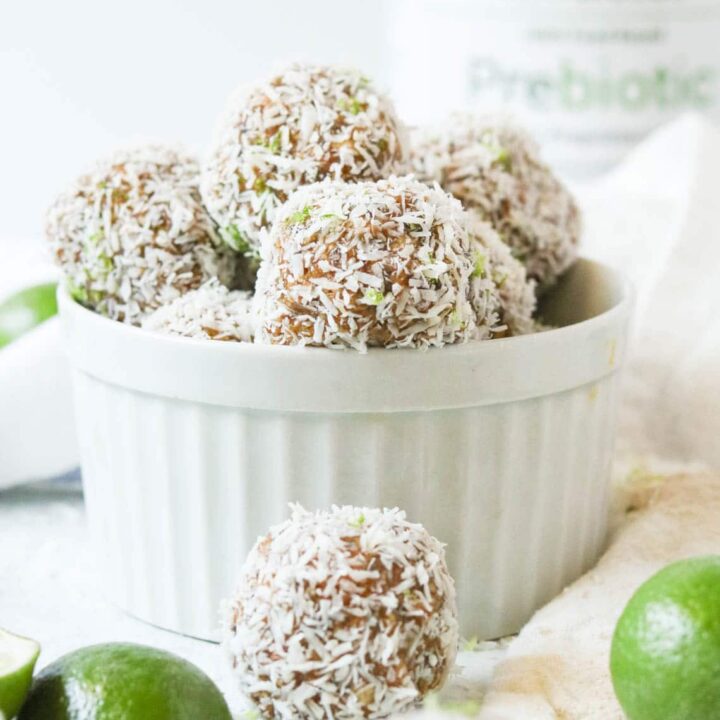 Key Lime Power Balls with Prebiotics sitting in a bowl next to a jar of Hyperbiotics Prebiotic powder and key lime wedges