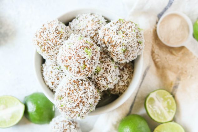 Key Lime Power Balls with Prebiotics sitting in a bowl next to a jar of Hyperbiotics Prebiotic powder and key lime wedges