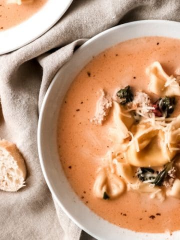 a bowl of creamy tomato tortellini soup with a sliced baguette sitting nearby