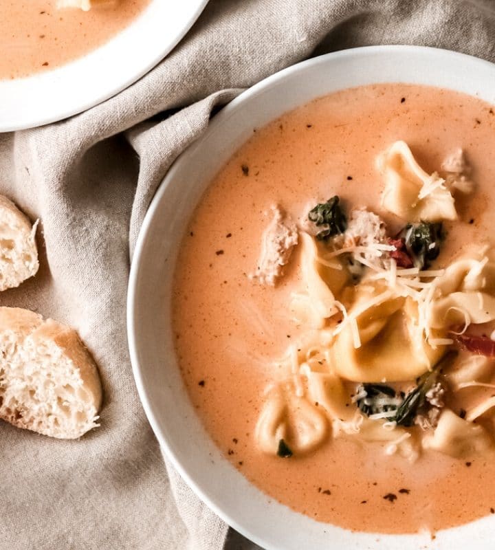 a bowl of creamy tomato tortellini soup with a sliced baguette sitting nearby