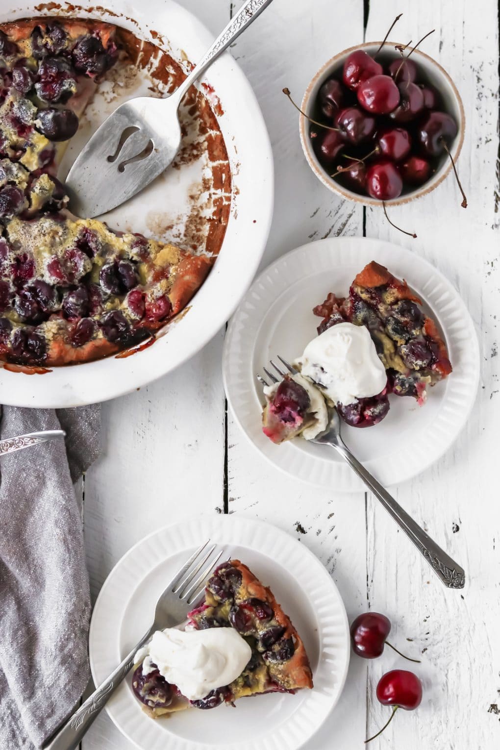 two slices of cherry clafoutis on plates with homemade whipped cream