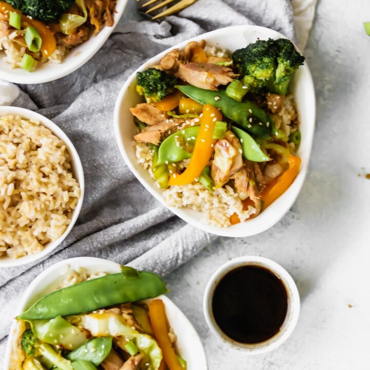 3 bowls of chicken stir-fry with one bowl of brown rice and a small bowl of sauce
