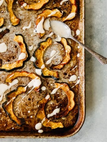 roasted acorn squash on a baking sheet, drizzled with maple aioli