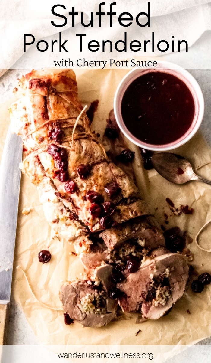 a stuffed pork tenderloin with a white bowl of cherry port sauce sitting to the right and a carving knife sitting to the left