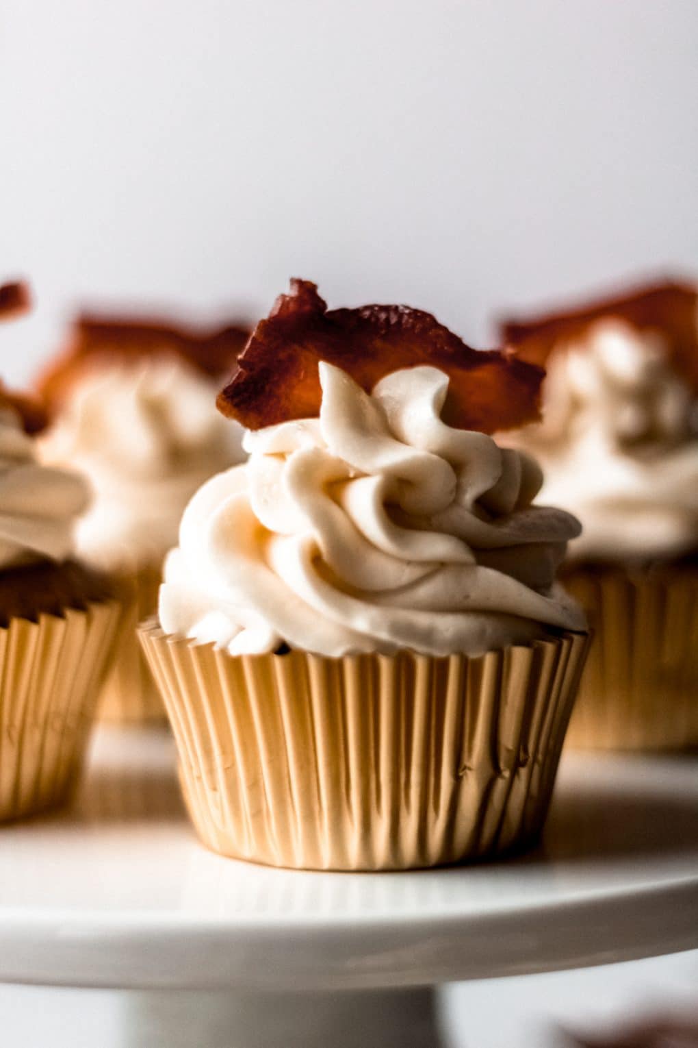 A close up shot of one maple bacon spice cupcake on a cupcake stand with additional cupcakes in the background