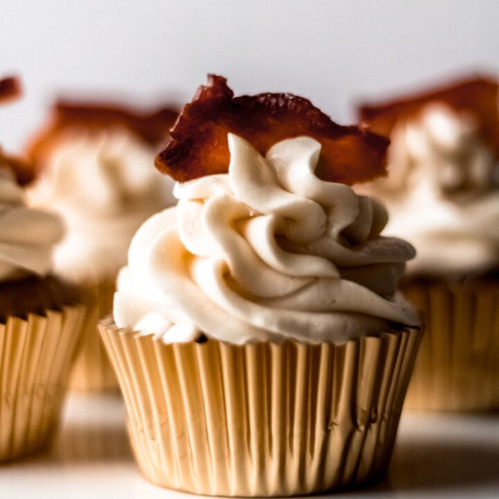 A close up shot of one maple bacon spice cupcake on a cupcake stand with additional cupcakes in the background