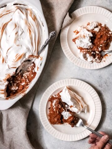 meringue-topped sweet potato casserole with two servings on a plate and a person holding a fork