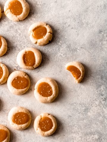 several salted caramel thumbprint cookies gathered on the left side of the image with the cookie with furthest to the right having a bite out of it