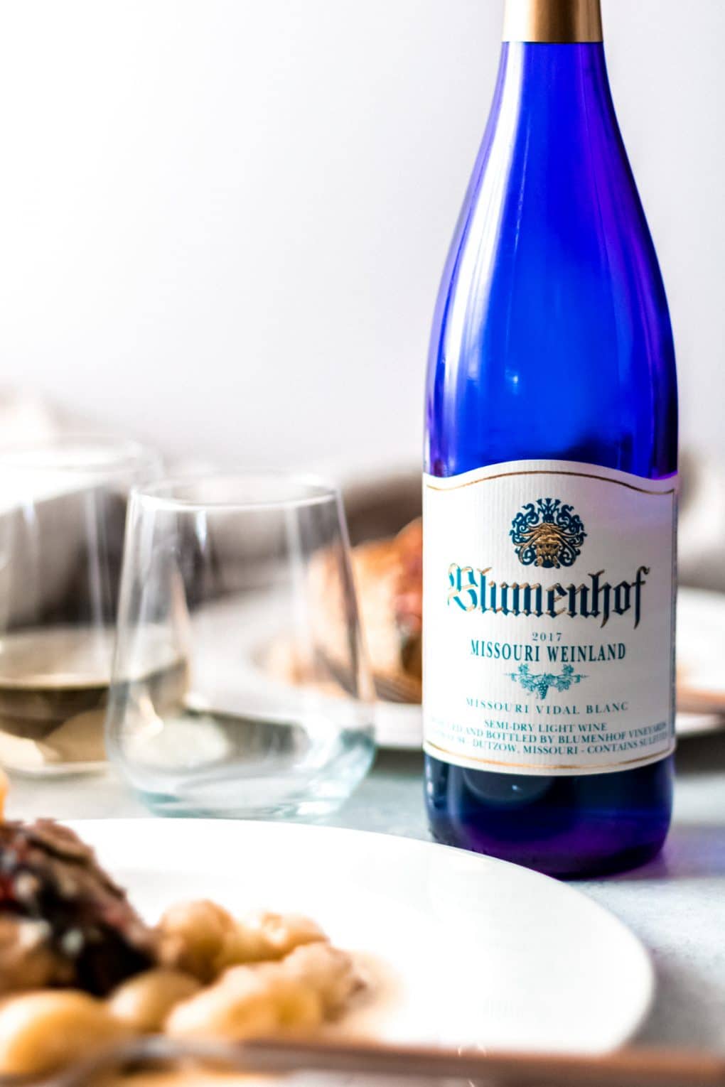 A blue bottle of Missouri Weinland vidal blanc wine with an empty wine glass to the left