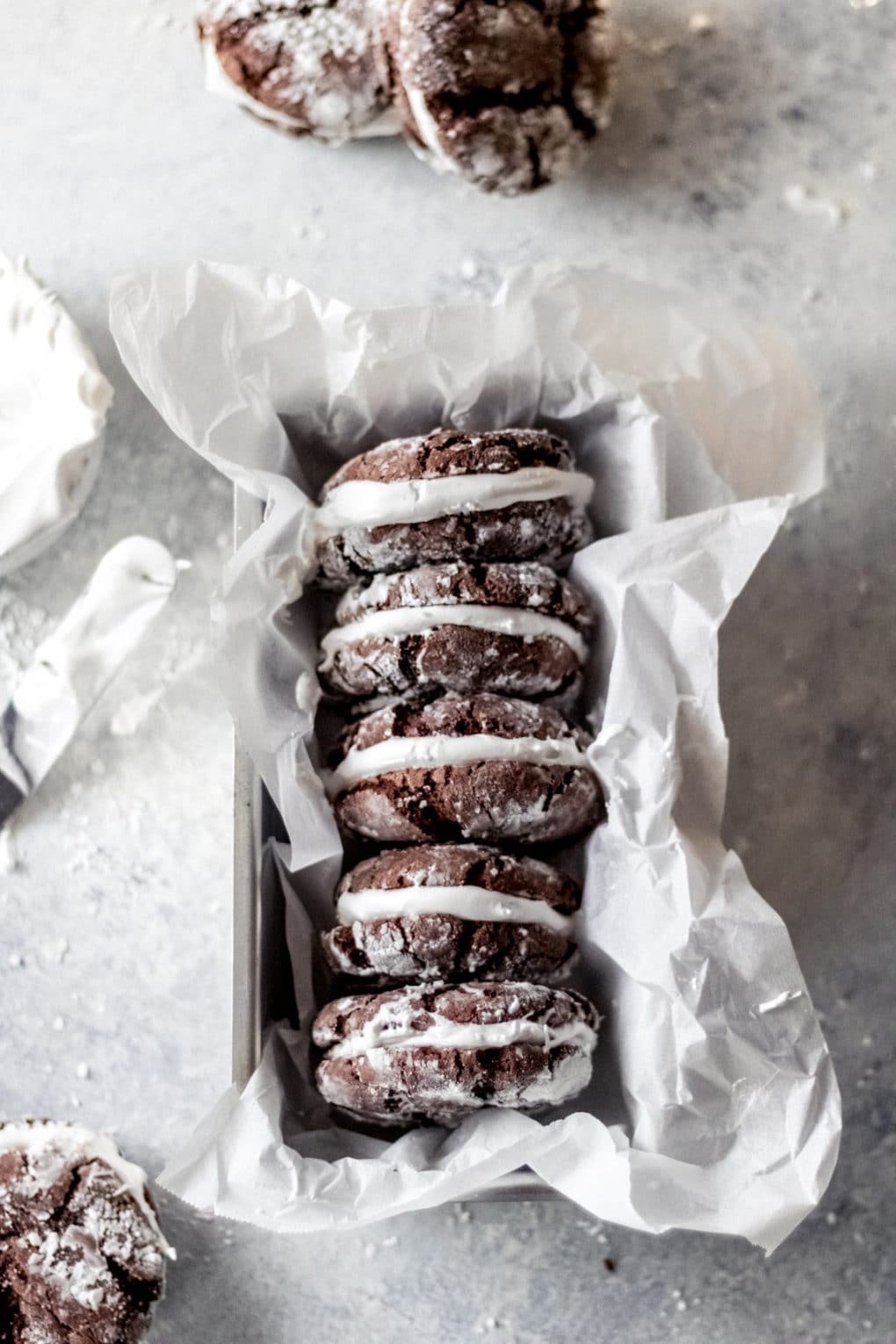 four hot cocoa sandwich cookies in a small baking tin lined with white parchment paper. 