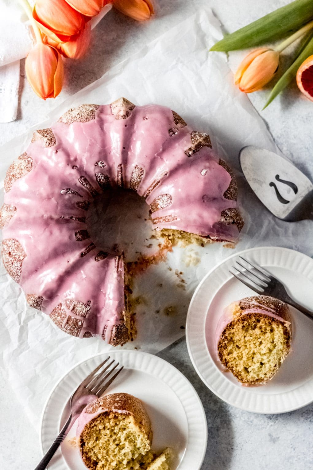 a blood orange olive oil cake with two slices cut and placed onto white plates. 