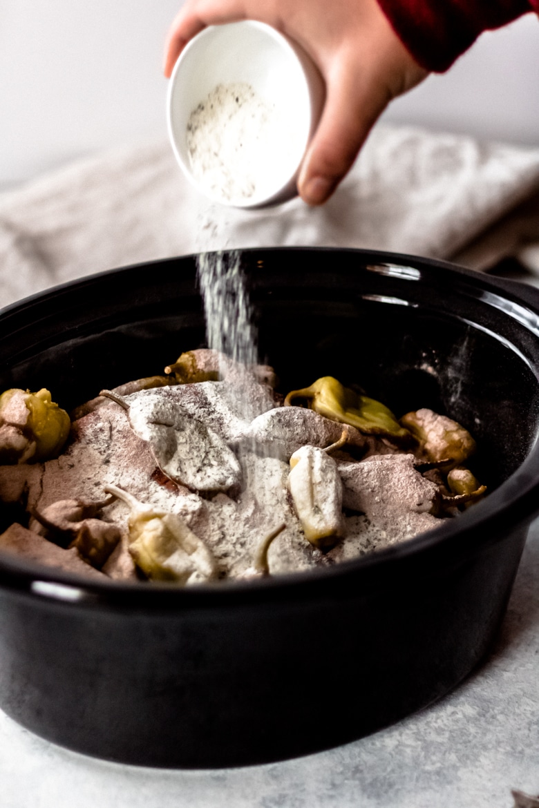 a person pouring the dried ranch mix over the Mississippi Pot roast in a black slow cooker crock