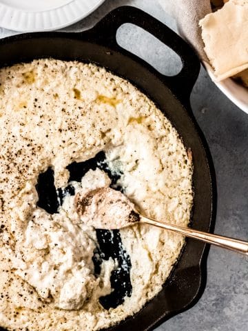 baked ricotta dip in a cast iron skillet. There's a gold spoon in the dish and you can see a basket of bread nearby.