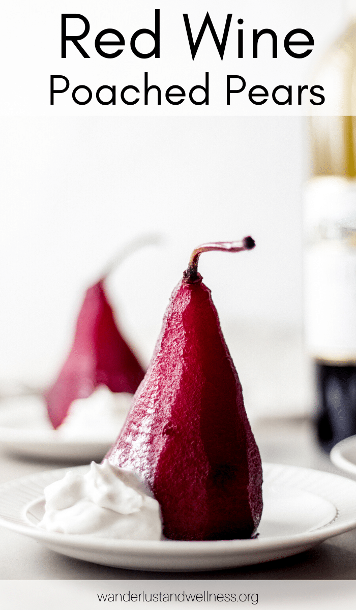 two red wine poached pears on a white plate with a bottle of wine in the background