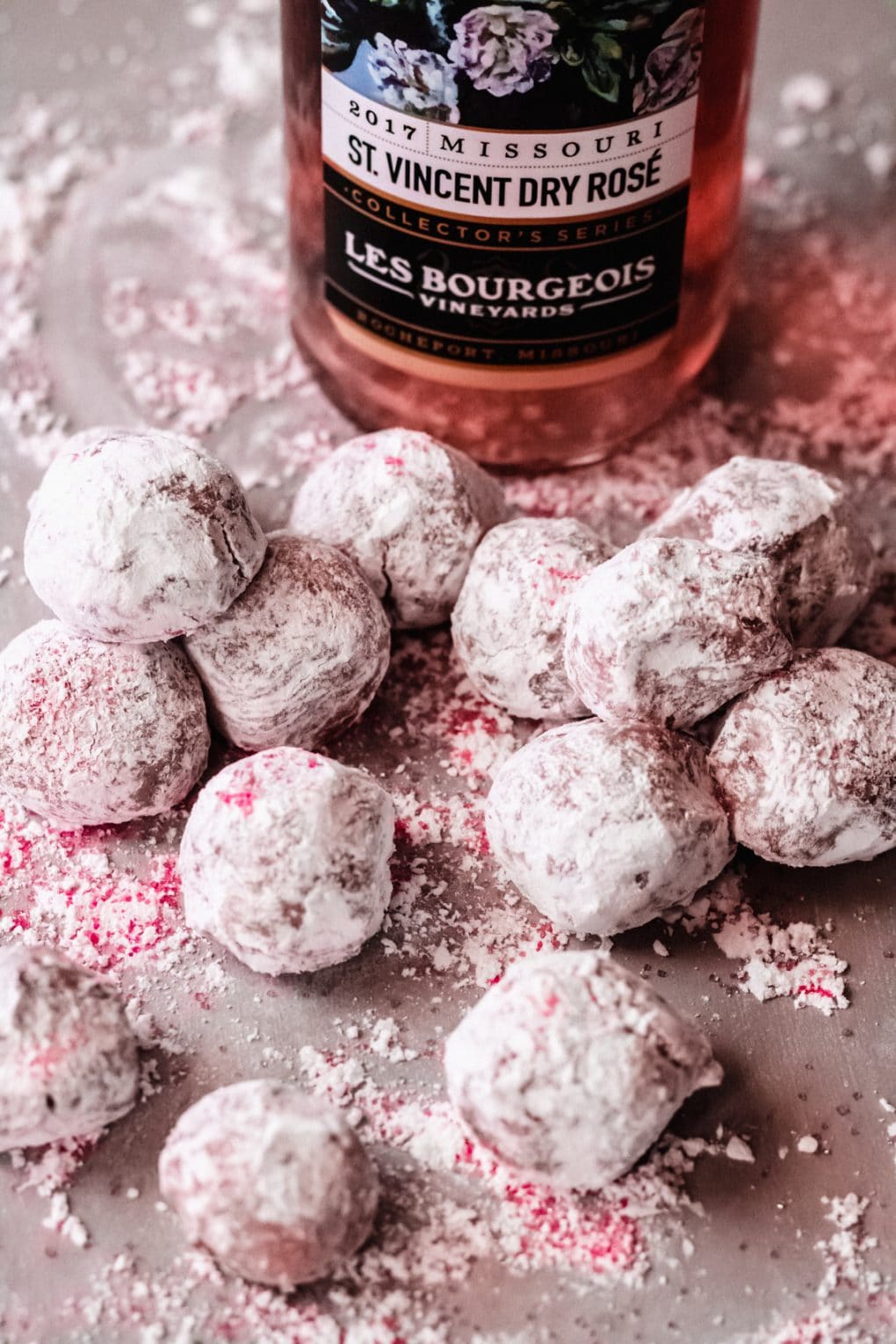 a pile of white chocolate rosé truffles on a table, there is a bottle of rosé in the background