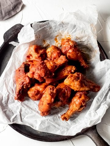 a pile of chicken wings on a sheet of white parchment paper sitting on a flat cast iron skillet