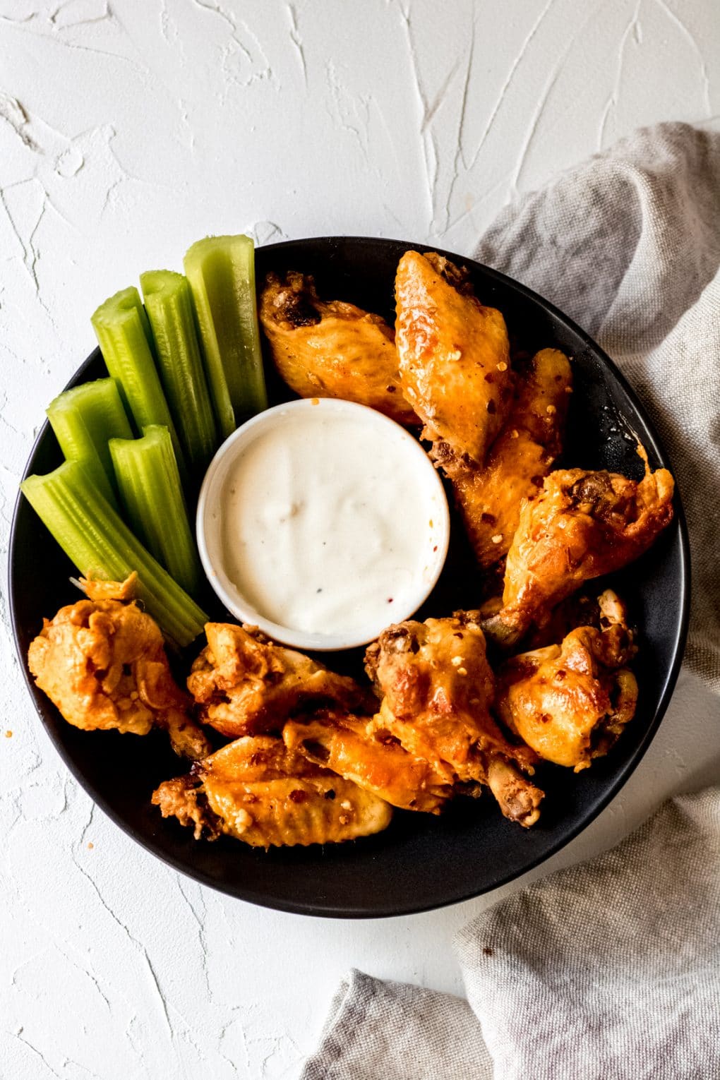 a black bowl with crock pot chicken wings, a bowl of blue cheese dressing, and celery