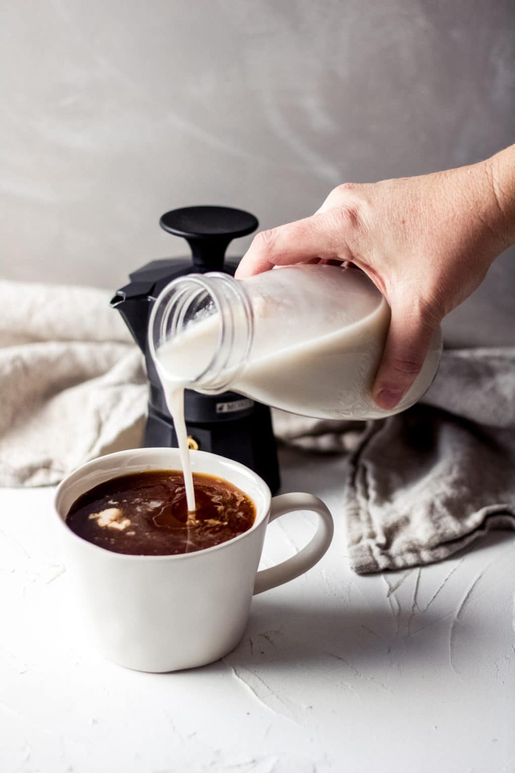 a woman pouring coffee creamer into a cup of coffee