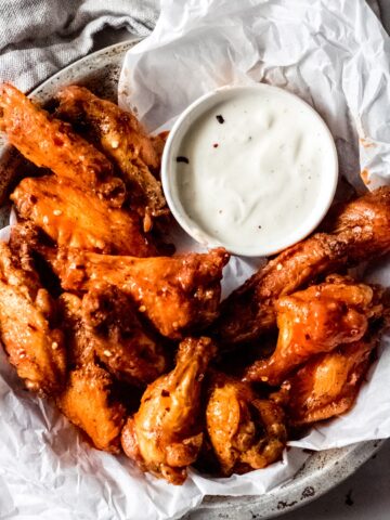 a bowl of hot spicy chicken wings sitting on white parchment paper and a bowl of blue cheese sauce