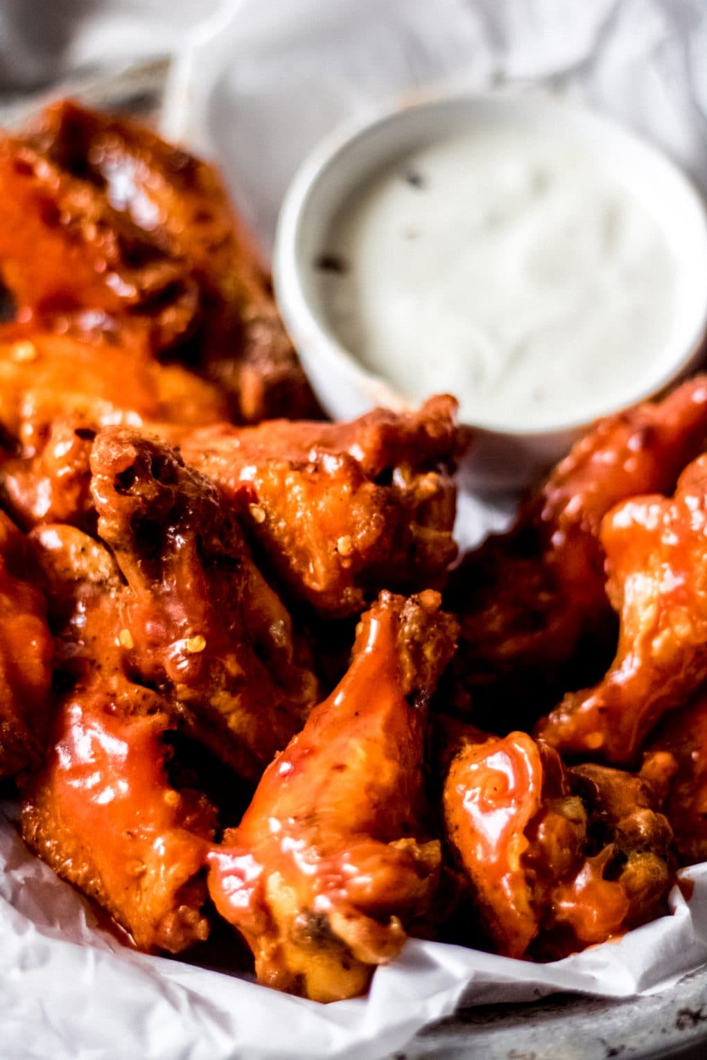 hot spicy chicken wings on white parchment paper with a bowl of blue cheese dressing