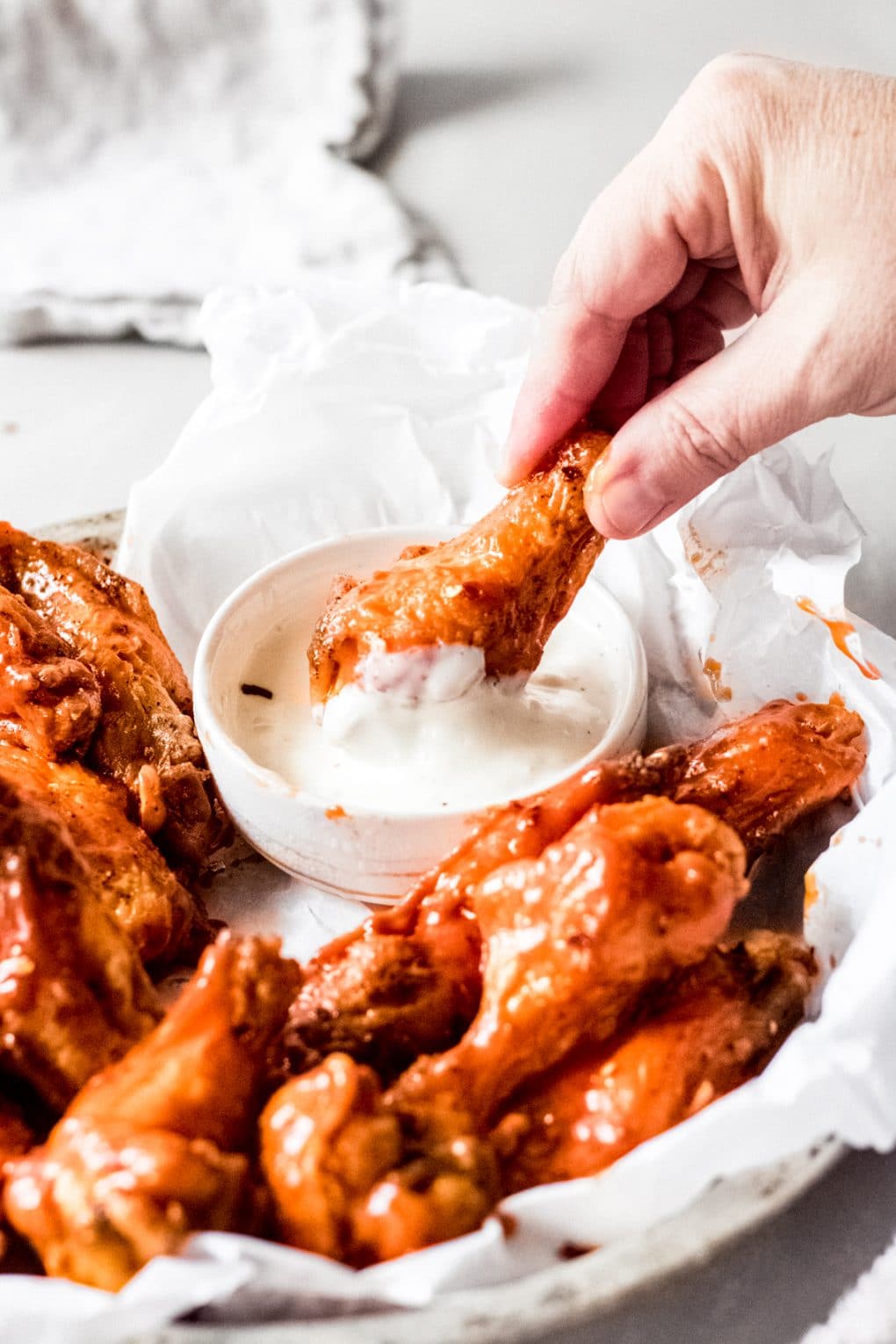 a woman dipping a hot spicy chicken wing into a bowl of blue cheese dressing