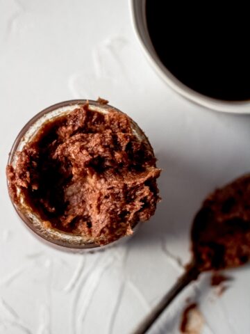 an overhead shot of mocha coconut oil coffee creamer in a small glass jar. There is a cup of coffee and spoon nearby