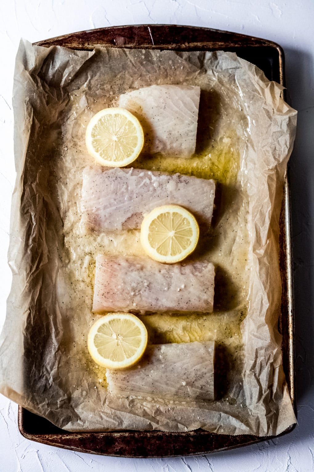 a baking sheet lined with parchment paper with four raw Mahi Mahi fillets and lemon slices