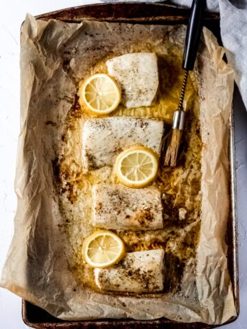a sheet pan covered in parchment paper with four Mahi Mahi fillets, melted butter, slices of lemon, and a basting brush