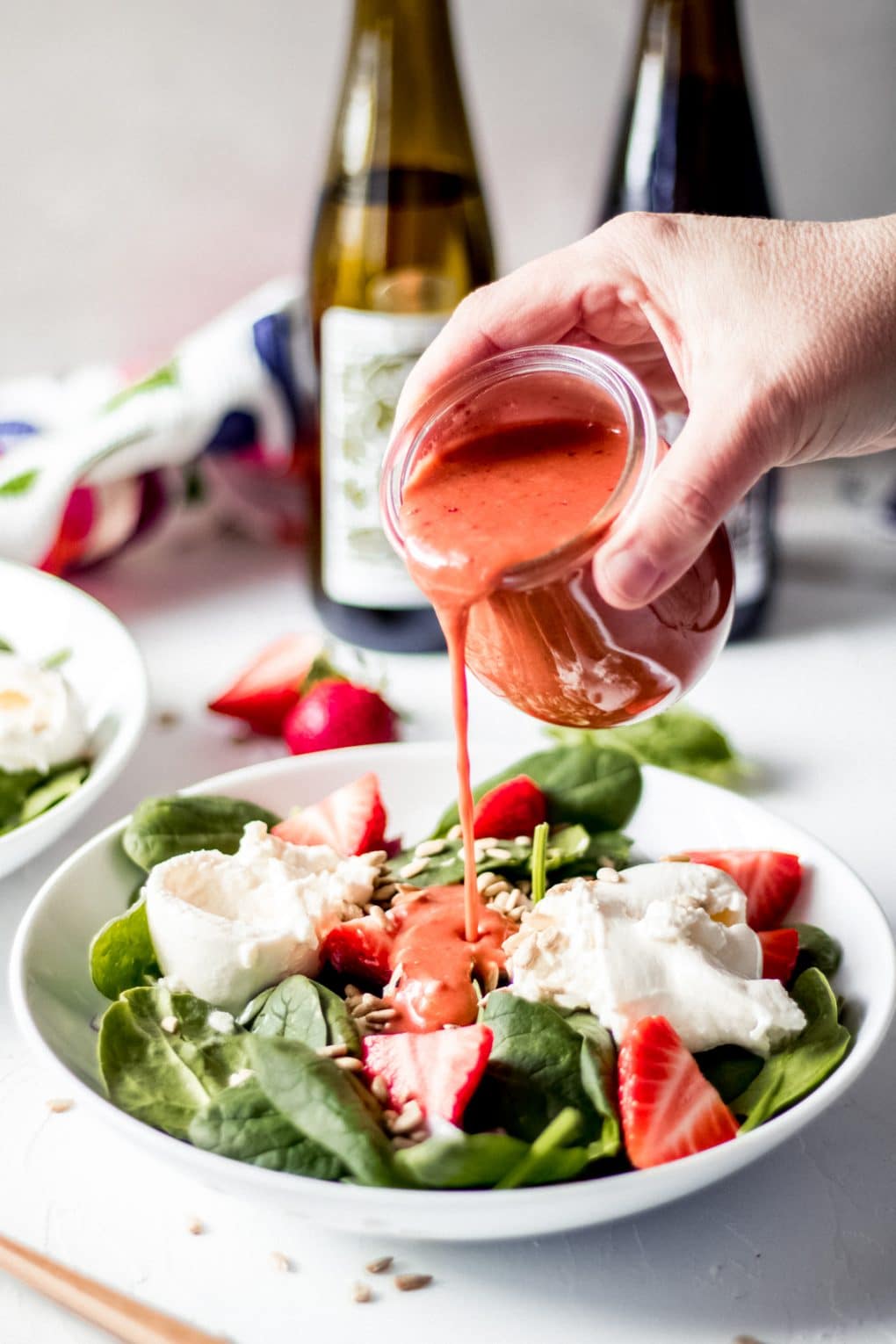 someone pouring strawberry basil homemade salad dressing over a strawberry basil burrata salad
