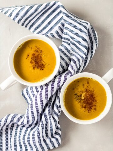 two mugs of bone broth turmeric latte - there is a navy striped towel draped between the mugs