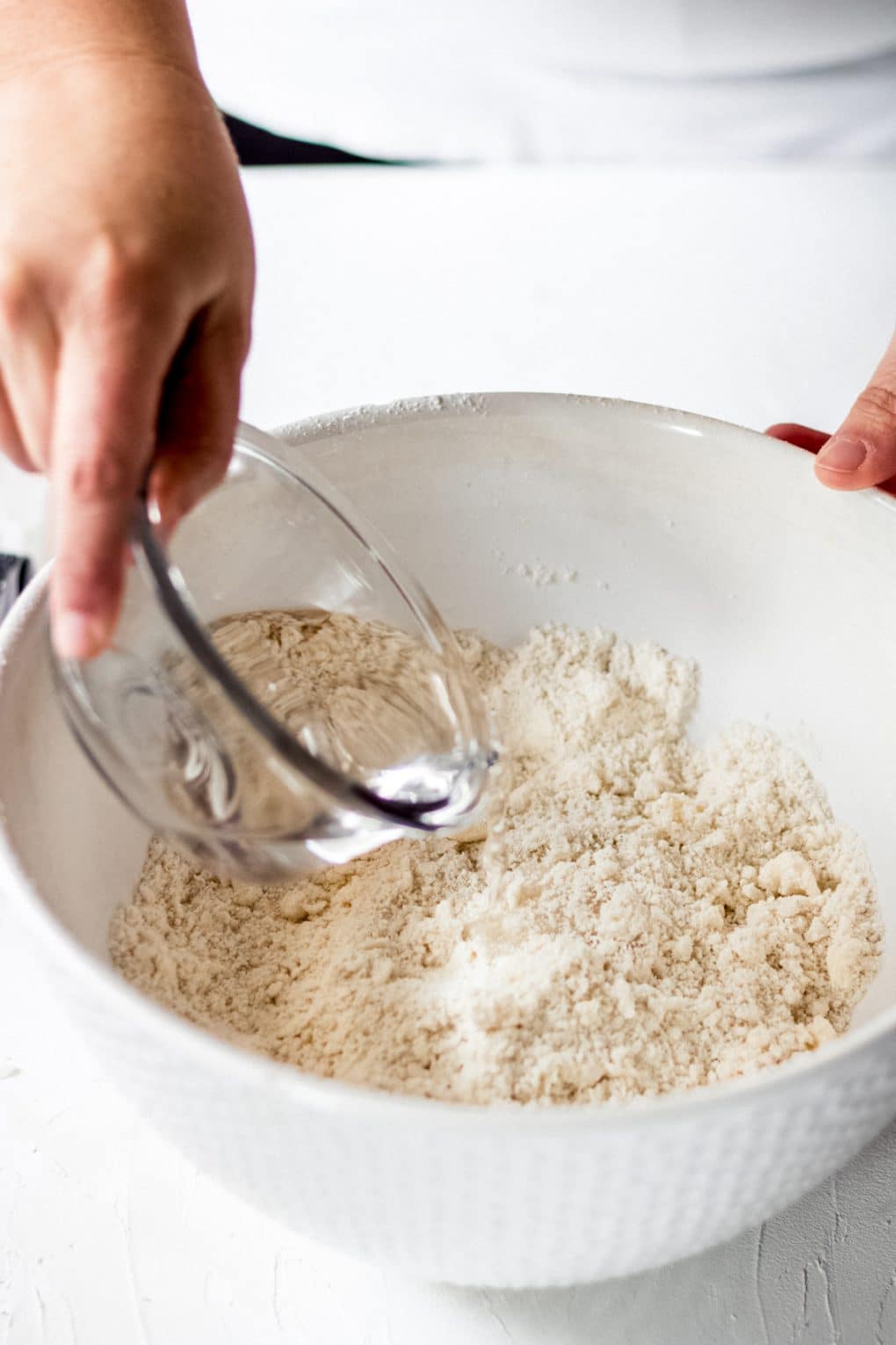 a woman pouring water onto the flour mixture