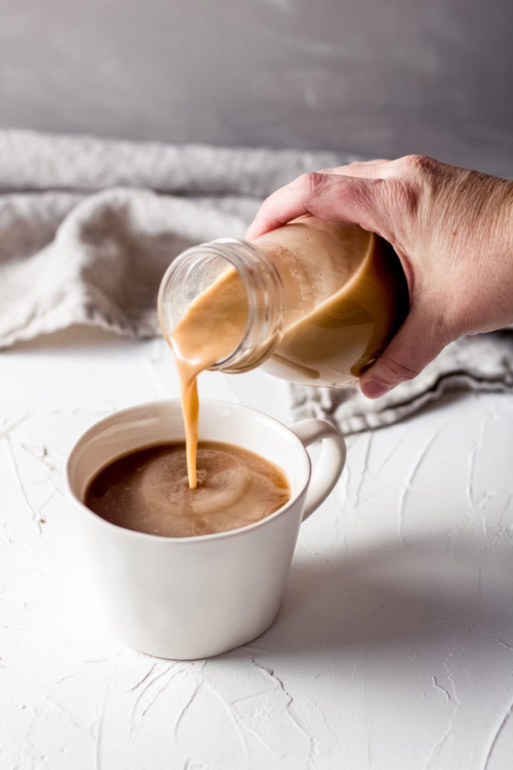 a woman pouring homemade dairy free salted caramel coffee creamer into a cup of coffee