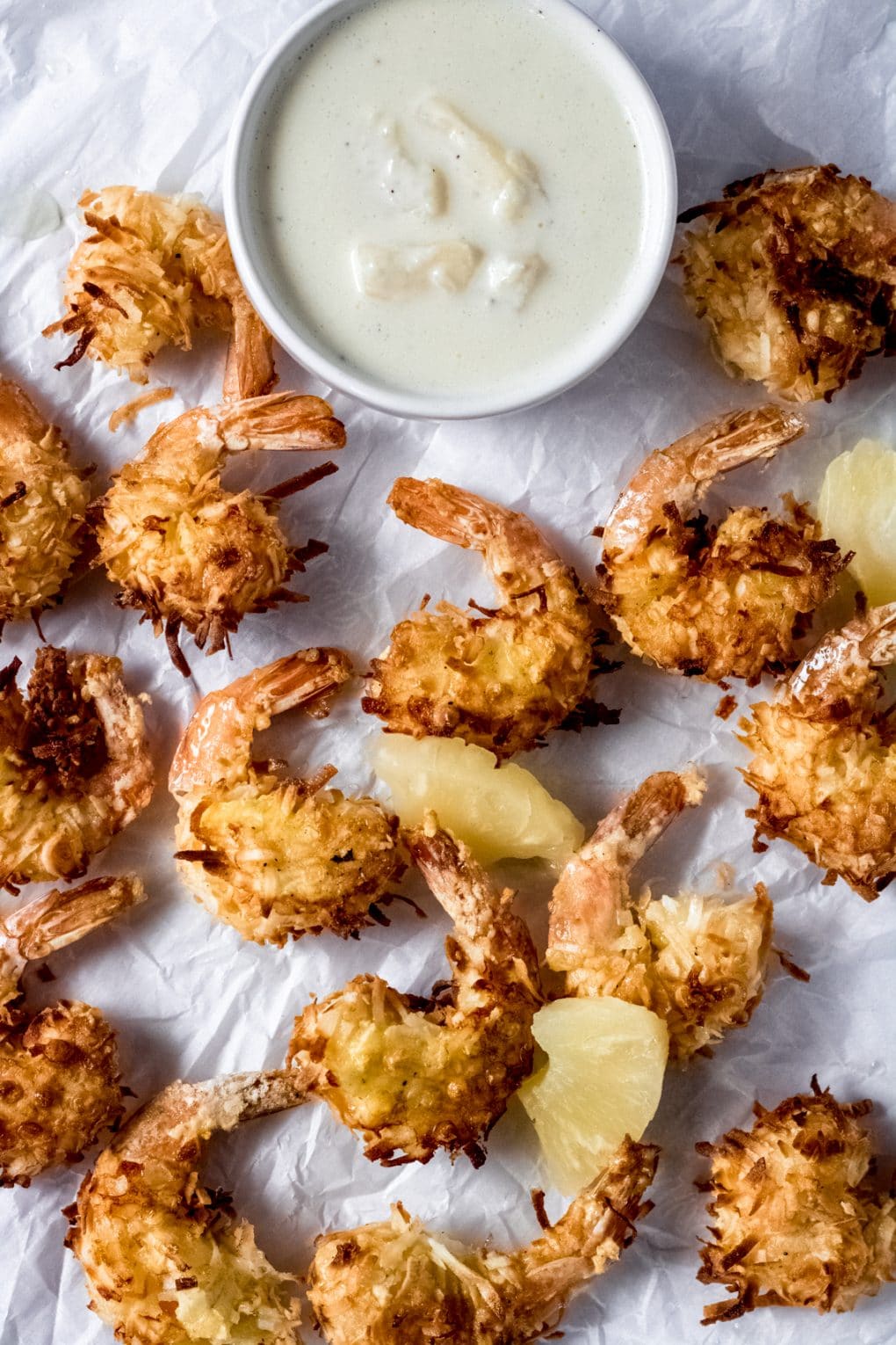 air fryer coconut shrimp on parchment paper with a bowl of pineapple aioli