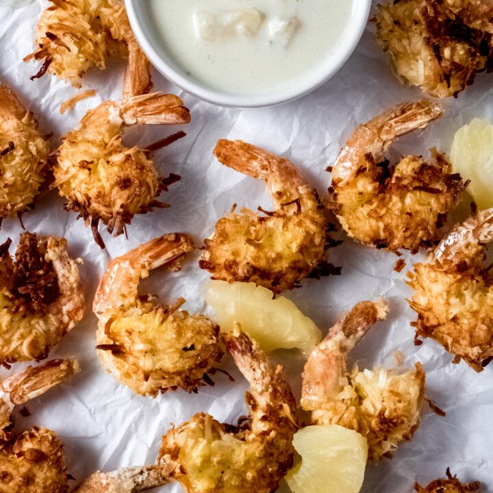 air fryer coconut shrimp on parchment paper with a bowl of pineapple aioli