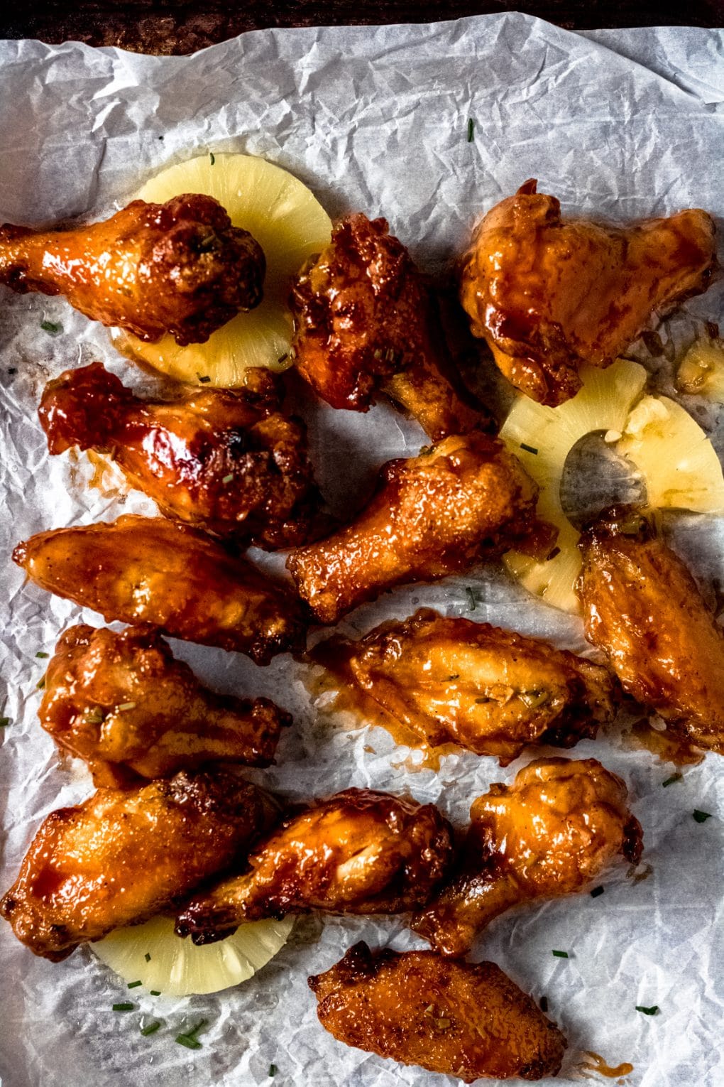gluten-free hawaiian style chicken wings and chunks of pineapple on a parchment paper lined baking sheet