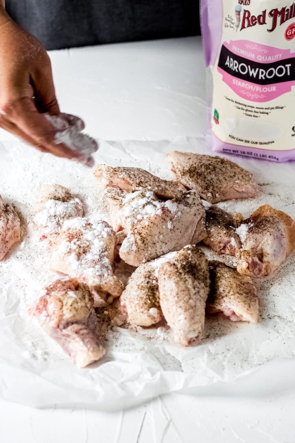 seasoning raw chicken wings with salt, pepper, and arrowroot starch