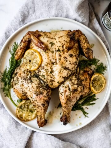 a whole grilled greek spatchcocked chicken on a white plate