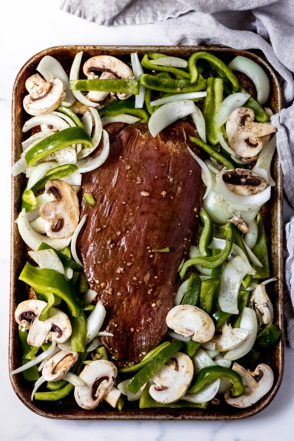 uncooked flank steak, onion, green peppers, and mushrooms on a sheet pan